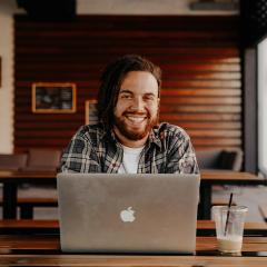 Man with dreadlocks in front of Apple Mac laptop smiles at camera