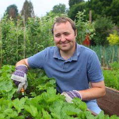 Gardener smiling to camera kneeling by bed of plants