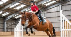 Equine student in a red top jumps on a horse over a fence