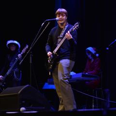 A man performing on stage with microphone and guitar