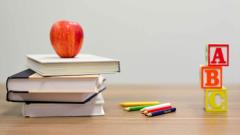 Stack of books with an apple on top of them, some colours pencils and ABC blocks all sat on a desk