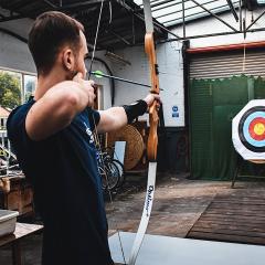 Man in blue t-shirt fires an arrow towards a target