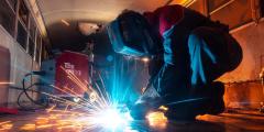 Someone in a protective mask and boiler suit welding metal with blue and yellow sparks flying