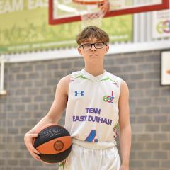 A young person holding a basketball under his right arm