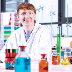 A student sat in a science lab with an array of brightly colours chemicals