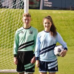 A male and female footballer posing for the camera, the lady has a ball under her arm