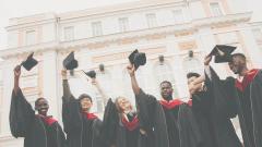 A row of six university gradates holding their mortar boards in the air