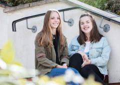 Two female students sat outside on some steps.