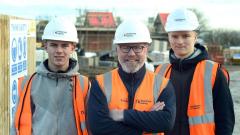 Three smiling men wearing high vis vests and hardhats at construction site