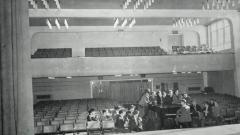 A black and white photo of the Easington College theatre hall with group singing and playing piano