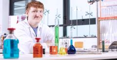 Smiling student in lab coat with chemistry equipment on lab desk