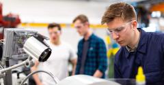 Engineer in goggles looking at robotics with two people in the background