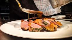 A closeup of a spoon pouring gravy over some pink meat