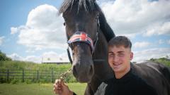 Jackson Black smiles at camera with a black horse wearing British flag bridle