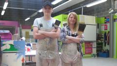 Two painting and decorating students in painting workshop pose with brushes and arms crossed