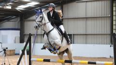 Rachel Murray jumps on a white horse over a white, yellow and black fence