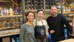 Rebecca Quinn posing with the two owners of Clean Bean restaurant with bottle of wine behind them