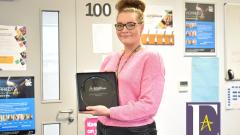 Sam Prince, wearing glasses and a pink jumper, holding her Peter Jones Enterprise Academy Award