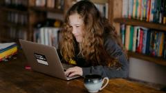 A teenager sat typing on a laptop, with a bookcase in the background