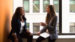 Two women sat in a windowsill smiling and having a chat