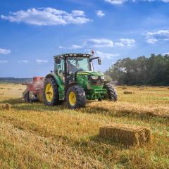 A green tractor harvesting hay in field on a sunny day