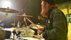 A long haired person, in a wholly hat, playing the drums