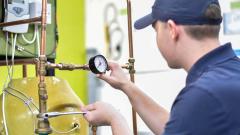 A man wearing a baseball hat, inspecting a dial on a boiler and using a spanner