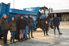 A group of six people stood next to a large blue trailer, attached to a tractor