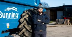 Young man with a beard and wearing a woolly hat stood next to a large blue vehicle with the word Bunning on its side in white lettering