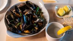 Mussels in a bowl, served on a wooden board with bread on the side