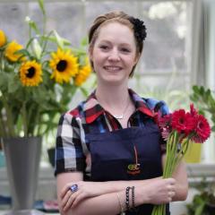 A female floristry student with arms crossed, holding flowers