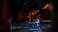 Welder in welding mask using a welding gun and creating sparks in a welding workshop