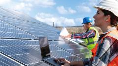 Woman in hardhat with laptop looking at solar panels