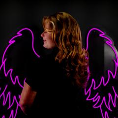 Red haired student standing in front of pink neon angel wings